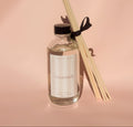 Creamsicle Reed Diffuser bottle with reeds on a pink background