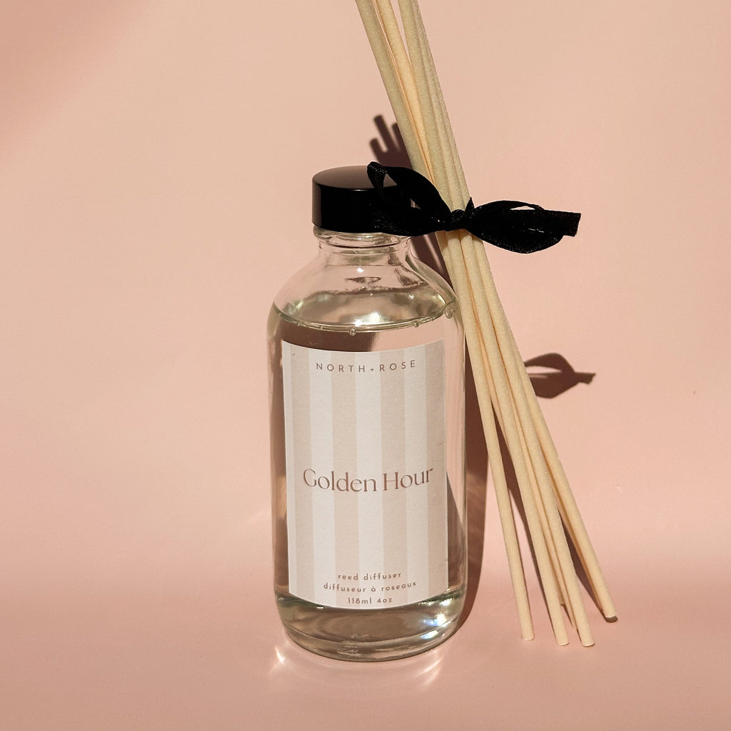 Reed diffuser with sticks labeled 'Golden Hour' on a soft pink background