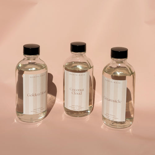 Three reed diffuser bottles of different scents on a pink background