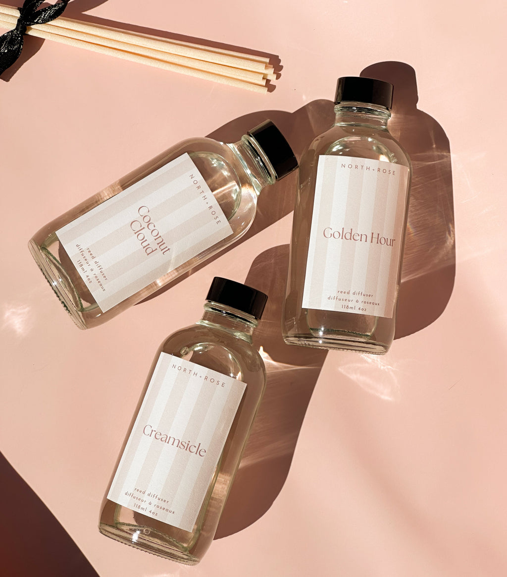 Three reed diffuser bottles of 'Golden Hour' and 'Creamsicle' on a pink background